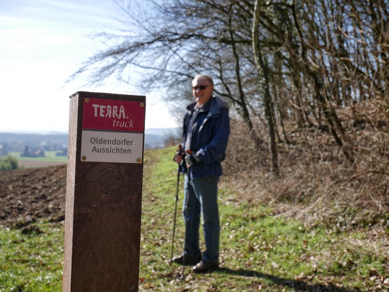 Wegweiser TERRA.track Oldendorfer Aussichten im Vordergrund, im Hintergrund unscharf ein Wanderer