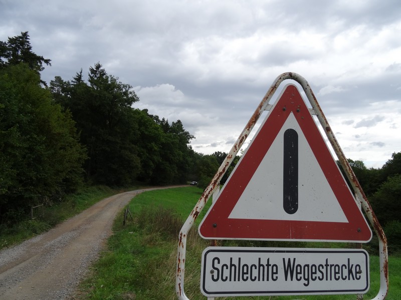 Das Bild zeigt ein Schild mit der Aufschrift "Schlechte Wegstrecke".