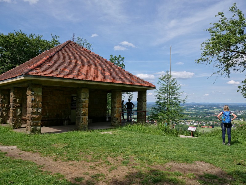 Das Bild zeigt links die Hütte der Schwedenschanze und rechts Meike, die die Aussicht genießt.